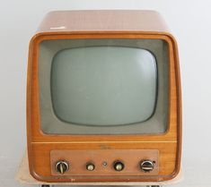 an old fashioned television sitting on top of a wooden stand in front of a white wall