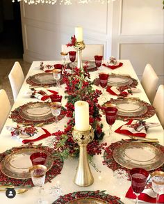 the table is set for christmas dinner with red and gold plates, silverware, and candlesticks