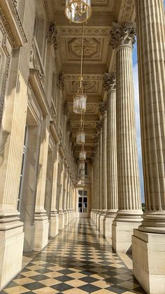 an empty hallway with columns and chandelier hanging from the ceiling in front of it