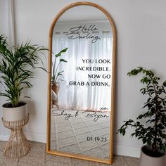 a mirror with a quote on it next to potted plants and a planter