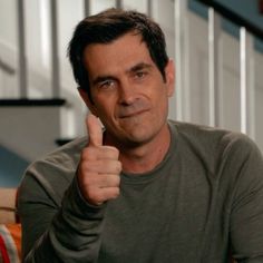 a man giving the thumbs up while sitting on a couch in front of some stairs