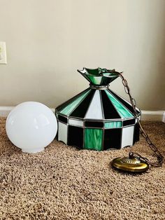 a green and white lamp sitting on top of a carpet next to a light bulb