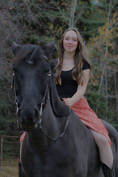 a young woman riding on the back of a black horse in front of some trees