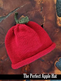 a red knitted hat sitting on top of a piece of wood with the words, the perfect apple hat written below it