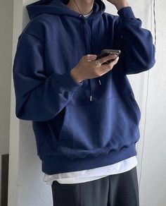 a man in a blue hoodie is holding a cell phone and listening to music