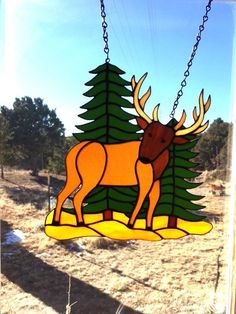 a stained glass deer ornament hanging from a chain in front of a window