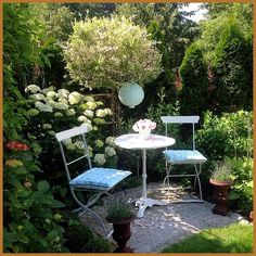 two chairs and a table in the middle of a garden