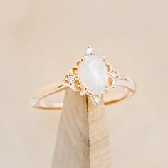 a gold ring with a white stone surrounded by small diamonds on top of a piece of wood