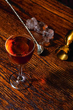 a close up of a wine glass on a table with spoons and ice cubes