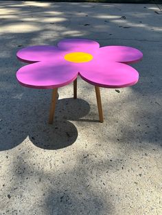 a purple flower shaped table sitting on top of a cement ground next to a tree