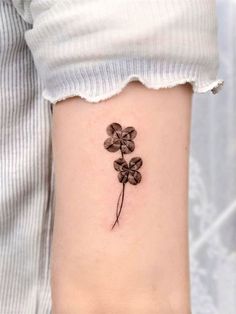 a small flower tattoo on the left side of the arm, with four petals attached to it