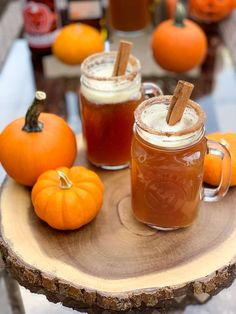 two mugs filled with liquid sitting on top of a wooden table next to pumpkins