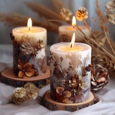 three candles with flowers on them sitting on a table next to pine cones and branches