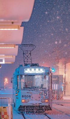 a snow covered train traveling down tracks next to a building and traffic light at night