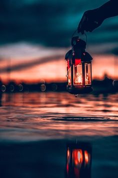 a person holding a lantern in the water at sunset or sunrise with their hand on it