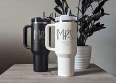 two travel mugs sitting on top of a table next to a potted plant