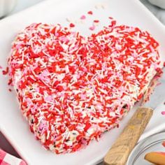 a heart shaped cake with sprinkles on a white plate next to other dessert items