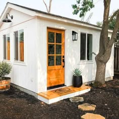 a small white house with an orange front door and wooden steps leading up to it