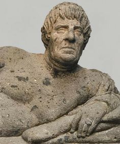 an old statue sitting on top of a cement slab in front of a gray sky