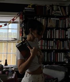 a woman standing in front of a bookshelf holding a book