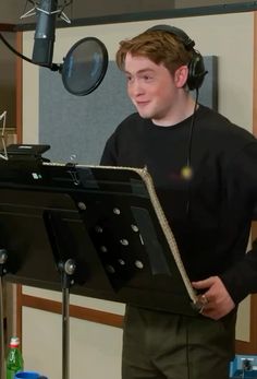 a young man wearing headphones standing in front of a microphone and holding a book