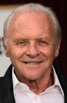 an older man with white hair smiles at the camera while wearing a black jacket and white shirt