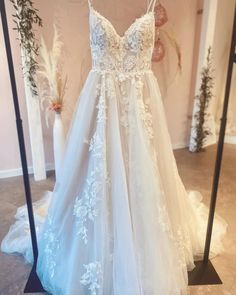 a white wedding dress hanging on a rack in front of a mirror with flowers and greenery