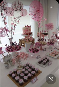 a table topped with lots of cupcakes and desserts covered in pink frosting