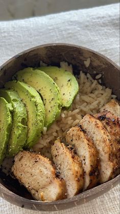 a bowl filled with rice, meat and avocado on top of a table