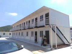 two people are standing in front of a white building with black balconies on the second floor