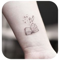 a small tattoo on the wrist of a person with an open book and stars flying out of it