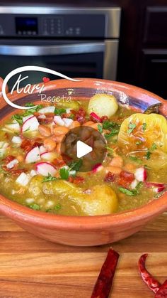 a bowl filled with soup sitting on top of a wooden table next to red peppers