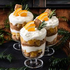 three desserts with orange slices and whipped cream on top, surrounded by greenery