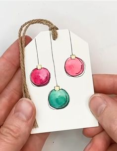 a hand holding a small tag with christmas ornaments painted on it and string attached to it