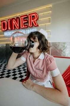 a woman sitting at a table drinking from a wine glass in front of a diner sign