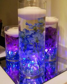 three candles are sitting on a table with purple flowers in the center and blue lights around them