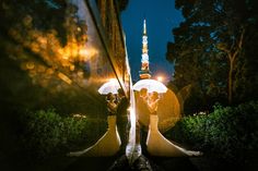 two people standing under umbrellas in the rain at night with trees and bushes behind them