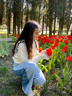 a woman kneeling down in front of a field of red tulips