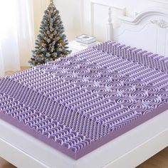 a bed with purple sheets and a christmas tree in the background