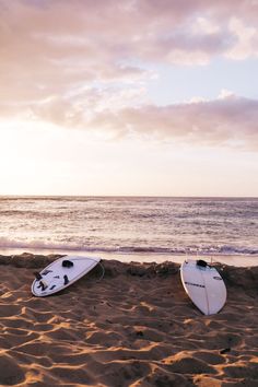 two surfboards sitting on top of a sandy beach next to the ocean under a cloudy sky