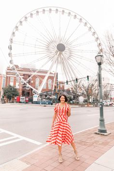 a woman in a red and white dress is standing on the sidewalk near a ferris wheel