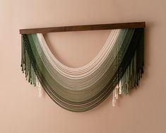 a wall hanging with green and white fringes on it's side next to a pink wall