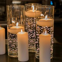 several lit candles sitting on top of a table next to glass vases filled with water