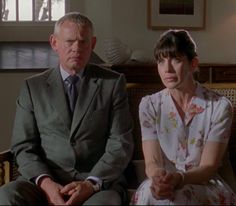 an older man and young woman sitting on a couch in front of a window looking at each other