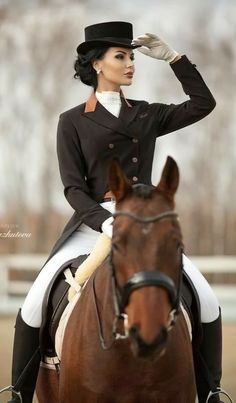 a woman riding on the back of a brown horse in a dressage suit and top hat