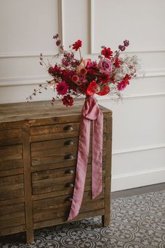 a bouquet of flowers sitting on top of a wooden dresser next to a white wall