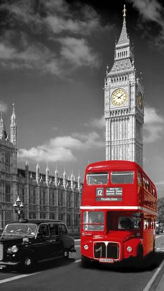 a red double decker bus driving down a street next to a tall tower with a clock on it