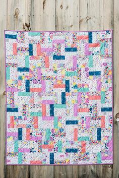 a colorful quilt is hanging on a wooden fence with the background painted in pastel colors