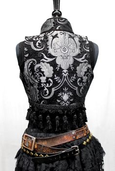 A beautiful bellydancer/burlesque style vest from the old country. A short vest with a stand-up collar in vintage european style, made in lush silver and black tapestry fabric with black satin lining inside. Exquisite black satin piping trim all over. Front fastens back with ornate metal medieval lion buttons or can be undone and crossed over worn double-breasted fashion. Elaborate black tassel trim at the bottom. Great for any bohemian affair. Comes in sizes Small-XXL. Splendid! Measurements: Small: Chest 32" Ribcage 30" Medium: Chest 34" Ribcage 32" Large: Chest 37" Ribcage 34" XL: Chest 40" Ribcage 37" XXL: Chest 43" Ribcage 40" Tapestry Vest, Black Tapestry, Style Vest, Vintage European, Short Vest, Tapestry Fabric, Belly Dancers, European Vintage, Rib Cage