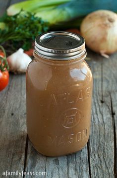 a jar filled with brown liquid sitting on top of a wooden table next to vegetables